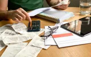 Person reviewing finances with receipts, smartphone calculator, and notepad at a table — symbolizing bankruptcy means testing.