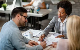 Three professionals at a meeting table—woman in gray suit pointing to documents while man and another woman listen attentively—symbolizing bankruptcy reaffirmation agreement discussions in Arizona