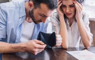 Worried couple examining an empty wallet and an unpaid bill, man in blue shirt and woman holding head in frustration, symbolizing bankruptcy decision stress in Arizona