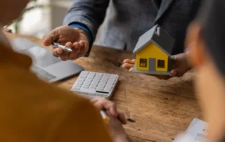 Person in suit holding yellow house model and pen at wooden table with laptop and calculator, symbolizing mortgage modification in Chapter 13