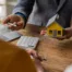 Person in suit holding yellow house model and pen at wooden table with laptop and calculator, symbolizing mortgage modification in Chapter 13
