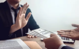 Person in suit extending cash while another in suit raises hand to refuse it, symbolizing integrity and rejection of bribery or wage garnishment workaround
