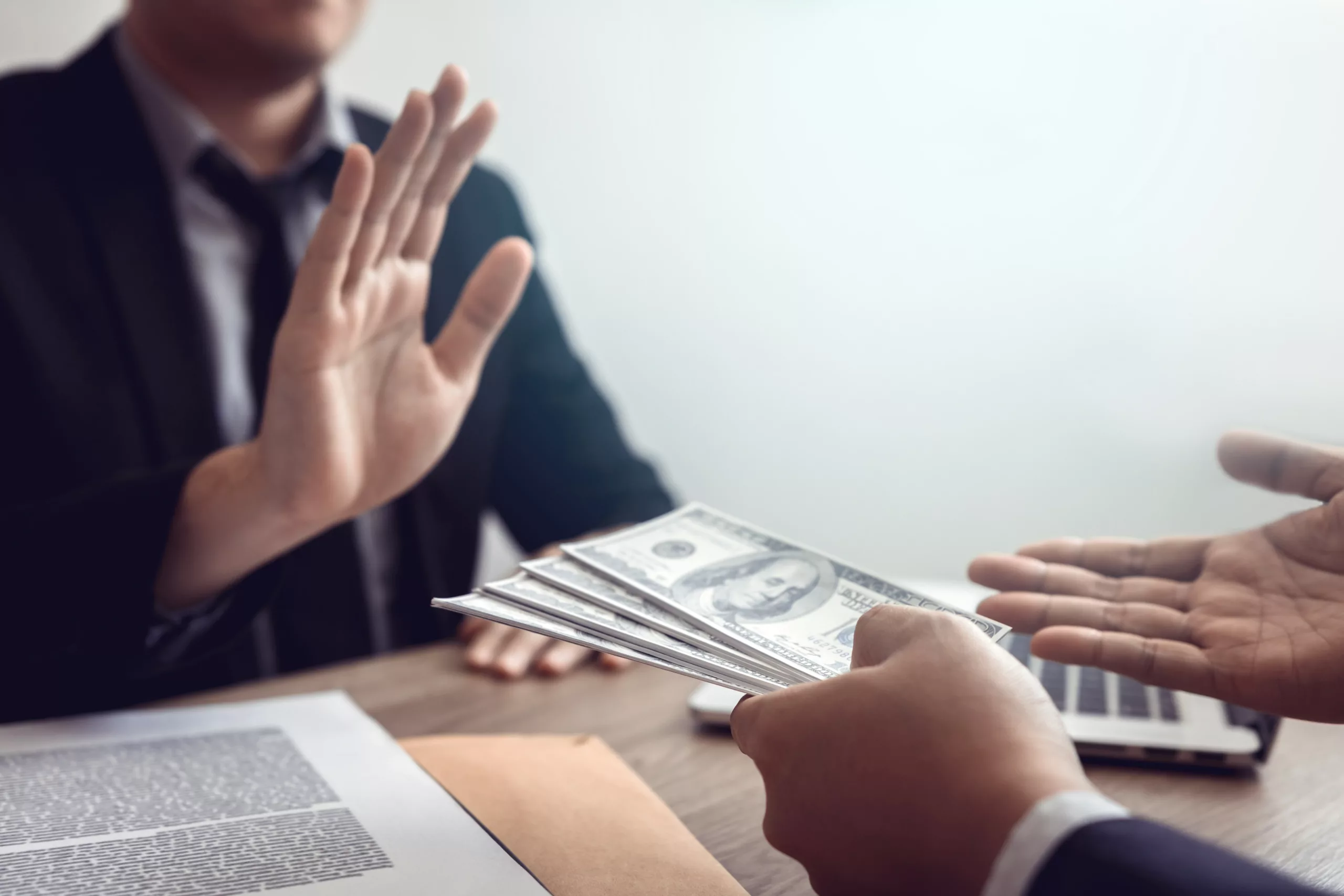 Person in suit extending cash while another in suit raises hand to refuse it, symbolizing integrity and rejection of bribery or wage garnishment workaround