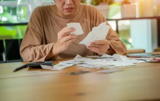 Person sitting at a wooden table sorting through receipts with a focused expression — illustrating the financial planning and debt review common in the context of deciding whether to file bankruptcy or divorce in Arizona.