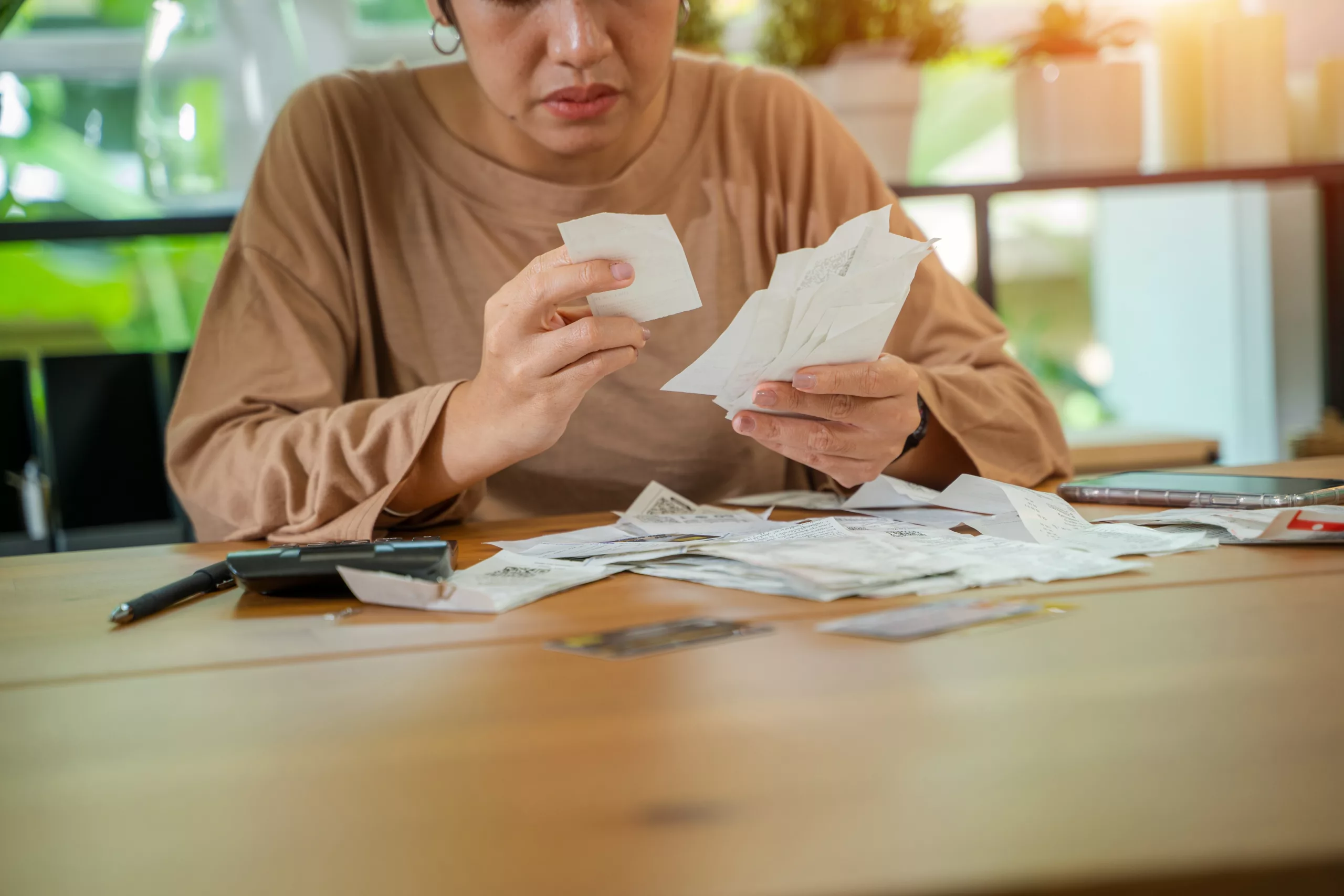 Person sitting at a wooden table sorting through receipts with a focused expression — illustrating the financial planning and debt review common in the context of deciding whether to file bankruptcy or divorce in Arizona.