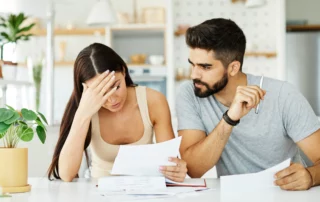 Worried couple reviewing bills at kitchen table, illustrating filing bankruptcy without a spouse in Arizona.